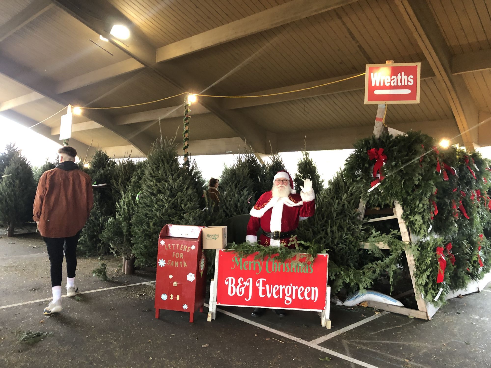 Santa waving from among fresh-cut trees and wreaths under the pavilion at the Richfield lot